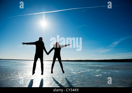 Teenager-Paar auf dem Eis auf einem gefrorenen See springen Stockfoto