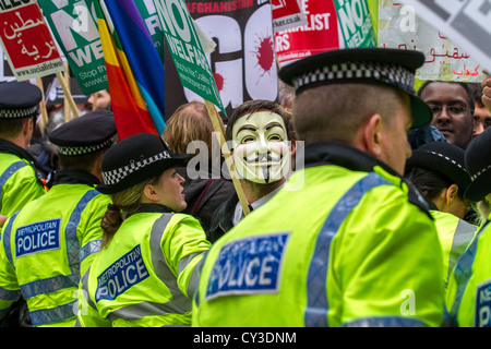 Ein maskierter Demonstrant bei Stop The War-Rallye in Trafalgar Square, London, Uk, blickt durch die Polizei umgeben. Stockfoto