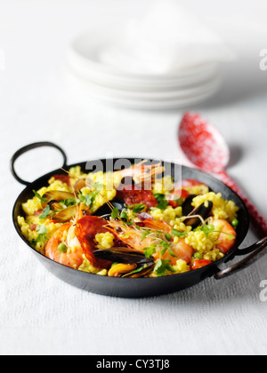 Paella mit Garnelen, Muscheln und Chorizo. Schuss auf ein weißes Tuch mit Platten im Hintergrund. Schwarz Metall Paella Schüssel Stockfoto