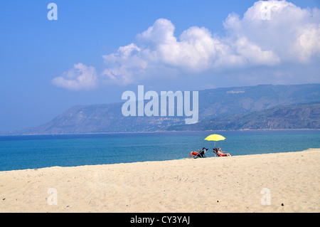 Zwei Personen sitzen auf Liegestühlen unter gelbe Sonnenschirm am Strand Stockfoto