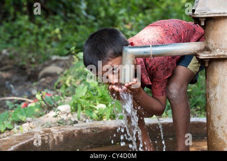 Junge indische Trinkwasser aus einer Handpumpe Wasser im indischen Dorf. Andhra Pradesh, Indien Stockfoto