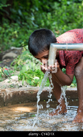 Junge indische Trinkwasser aus einer Handpumpe Wasser im indischen Dorf. Andhra Pradesh, Indien Stockfoto