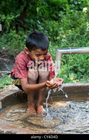 Junge indische Trinkwasser aus einer Handpumpe Wasser im indischen Dorf. Andhra Pradesh, Indien Stockfoto