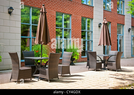 Patio-Möbel mit Sonnenschirmen auf steinernen Terrasse in der Nähe von gehobenen Eigentumswohnung Gebäude Stockfoto