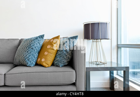 Raumgestaltung mit Couch, bunten Kissen und Lampe auf Tisch Stockfoto