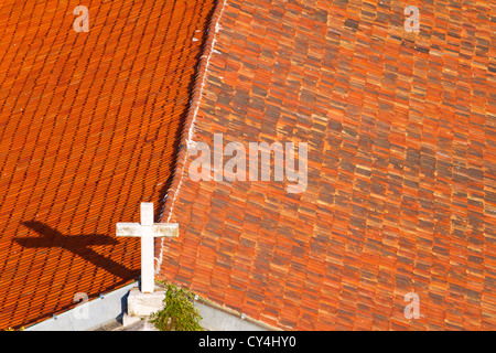 Kreuz auf der Kirche auf dem Dach mit orange Fliesen bedeckt Stockfoto