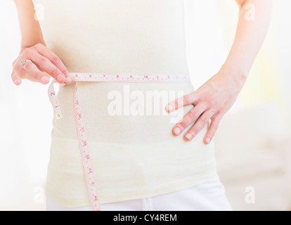 Junge Frau mit Maßband um die Taille gewickelt Mittelteil Stockfoto