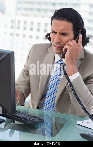 Porträt eines verwirrt Geschäftsmann mit einem Monitor arbeiten, während Sie auf dem Telefon Stockfoto