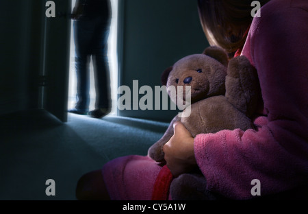 Rückansicht, wenn ein Kind in einem dunklen Raum mit einem Teddybär, ein Mann gerade den Raum verlassen hat. Stockfoto