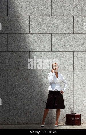 Mitte Erwachsene kaukasischen Geschäftsfrau telefonieren mit Handy und warten in der Nähe von Bürogebäude Wand. Textfreiraum Stockfoto