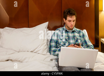 Ein junger Mann auf seinem Bett entspannen und mit seinem Laptop. Stockfoto