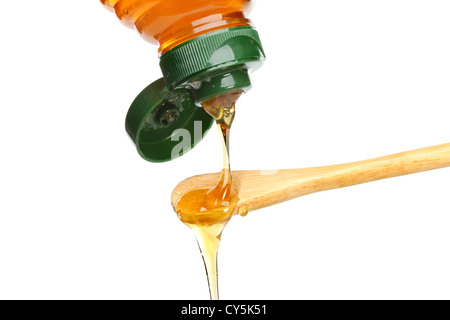 Honig aus einer Flasche auf einem Holzlöffel isoliert gegen weiß Gießen Stockfoto
