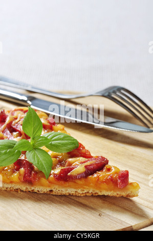 Stück Pizza mit Messer und Gabel auf Holzbrett Stockfoto