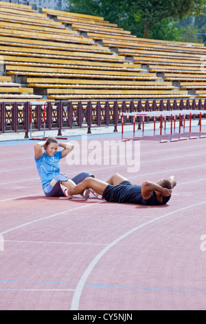 Zwei Athleten helfen einander, um die Bauchmuskeln im Stadion an einem sonnigen Tag crunch Stockfoto