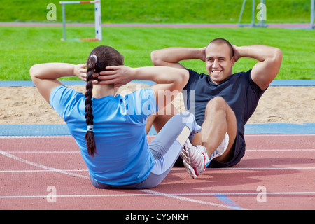 Zwei Athleten helfen einander, um die Bauchmuskeln im Stadion an einem sonnigen Tag ausüben Stockfoto