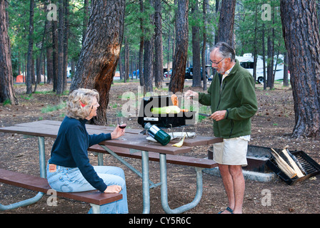 Man kocht Huhn und Mais auf tragbaren Grill auf Picknick-Tisch, während Frau am North Rim, Grand Canyon Campground sieht Stockfoto