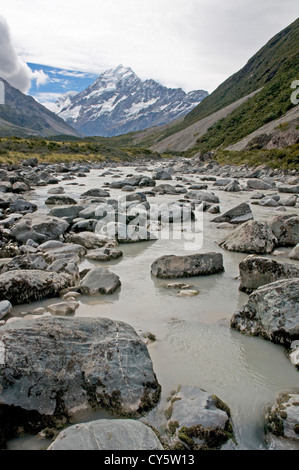 Eiskalte Wasser fließt entlang der Hooker Valley stromabwärts des Hooker-Gletschers, mit der majestätischen Gipfel des Mt. Cook in der Ferne Stockfoto