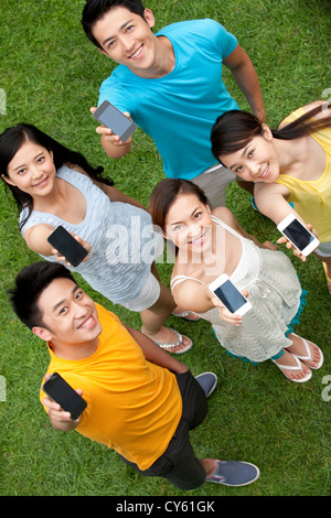 junge Menschen, die Mobiltelefone auf Wiese Stockfoto