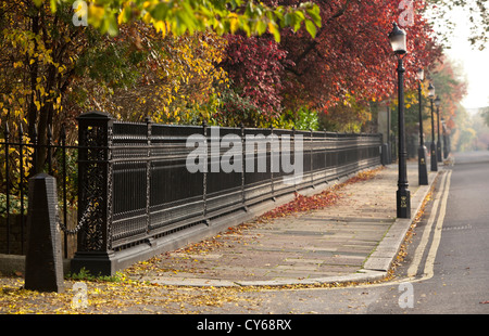 Einen Metallzaun und Reihe der Lampe Beiträge auf einem Gehsteig auf der Äußere Kreis des Regent's Park, London, England, UK. Stockfoto