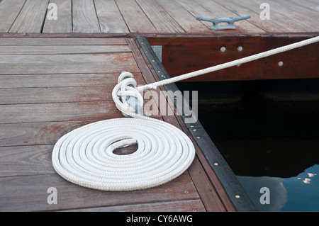 Weißen Seil aufgewickelt auf einem hölzernen Dock und gebunden an ein Metall Dock Klampe. Stollen dienen zur Sicherung der Docks und Linien von Booten Stockfoto