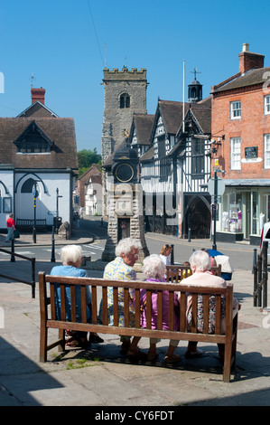 Vier Freunde sitzen auf einer Bank in Much Wenlock, Shropshire Stockfoto