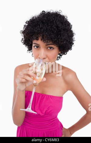 Junge Frau trinkt ein Glas Champagner vor einem weißen Hintergrund Stockfoto