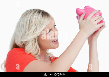 Blondine schüttelt ein rosa Sparschwein Stockfoto