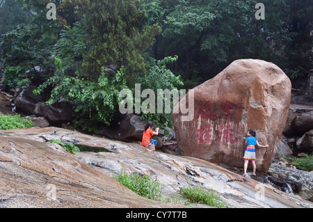 Zwei Mädchen stellen neben einem riesigen Boulder und seine Inschrift auf Tai in der Provinz Shandong, China Stockfoto