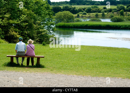 älteres Ehepaar sitzt auf der Bank Cosmeston Seen Land Park Penarth Vale von Glamorgan Süd wales uk Stockfoto