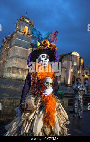 Eine kostümierte Dame mit einem Mais Schale Rock belebt die Atmosphäre in der Nähe der Kathedrale in Oaxaca, Mexiko. Stockfoto