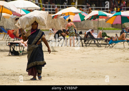 Horizontale Ansicht einer indischen Frau, die mit einer Tasche von Müll auf dem Kopf entlang dem Strand von Kovalam. Stockfoto