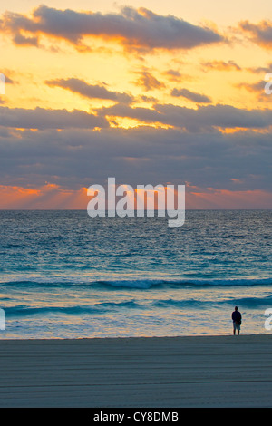 Person, die an einem Strand gerade Morgen Sonnenstrahlen brechen durch die Wolken (Hochformat) Stockfoto
