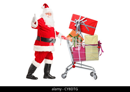 Santa Claus schieben einen Einkaufswagen voller Geschenke und einen Daumen aufgeben isoliert auf weißem Hintergrund Stockfoto