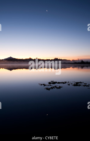 Sonnenaufgang im Nebel See Cassidy mit Mount Pilchuck Reflexionen und Halbmond Stockfoto