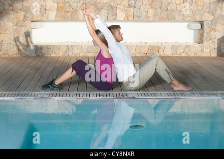 Junges Paar sitzen Rücken an Rücken am Pool erstreckt sich Stockfoto