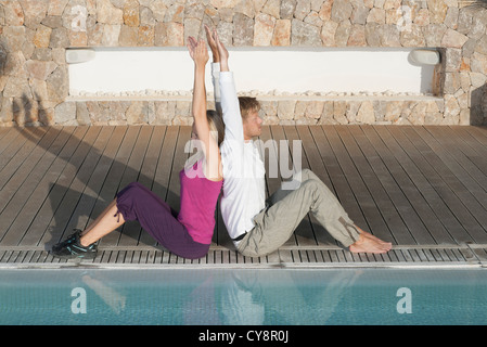 Junges Paar sitzen Rücken an Rücken am Pool, erhobenen Armen Stockfoto