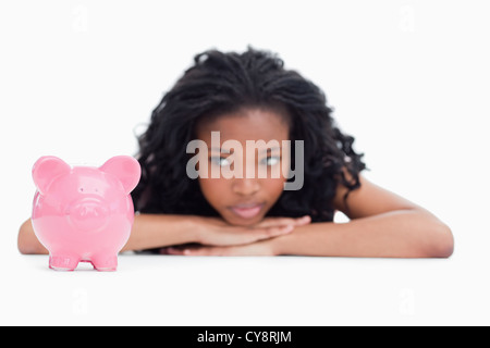 Junge Frau im liegen den Kopf auf den Händen ruhen blickt auf ein Sparschwein Stockfoto