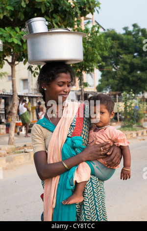 Armen niedrigere Kaste indische Frau mit Baby mit einem Topf Reis auf dem Kopf. Andhra Pradesh, Indien Stockfoto