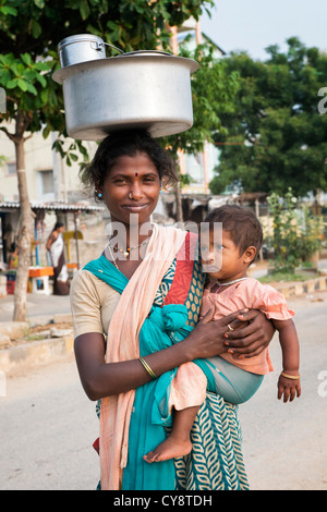 Armen niedrigere Kaste indische Frau mit Baby mit einem Topf Reis auf dem Kopf. Andhra Pradesh, Indien Stockfoto