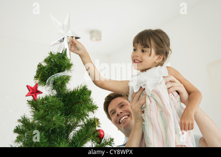 Vater tragen kleine Mädchen setzen Sterne an Spitze des Weihnachtsbaumes Stockfoto