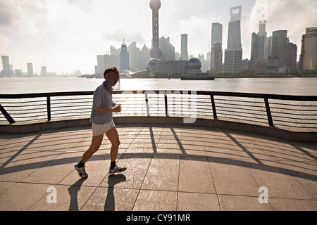 Ein Mann joggt am frühen Morgen auf den Bund gegen die Skyline des modernen Shanghai, China Stockfoto