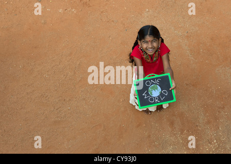 Indianerdorf Mädchen mit ONE WORLD geschrieben auf einer Tafel in einem indischen Dorf. Andhra Pradesh, Indien. Kopieren Sie Raum. Stockfoto