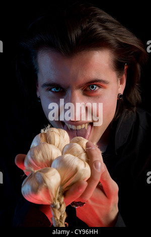 Vampir mit beängstigend Augen leckt Knoblauch, roten Horror Licht, auf schwarzem Hintergrund isoliert Stockfoto