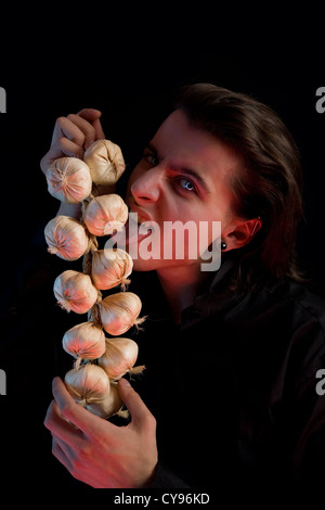 Vampir mit beängstigend blauen Augen ist lecken Knoblauch, roten Horror Licht, auf schwarzem Hintergrund isoliert Stockfoto