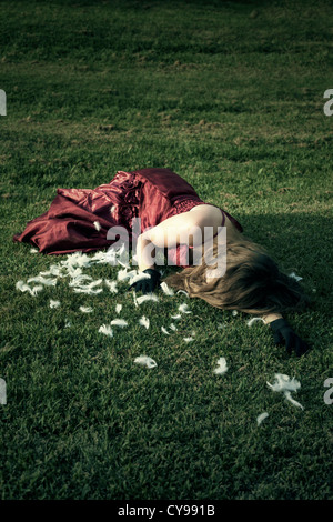 eine Frau in einem roten Kleid liegt auf einer Wiese unter Federn Stockfoto