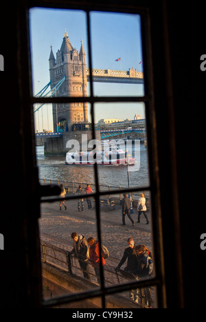 Tower Bridge bei Sonnenuntergang, Thames River cruise Boot und Touristen, angesehen durch alte verbleites Lichtfenster im Tower Of London UK Stockfoto