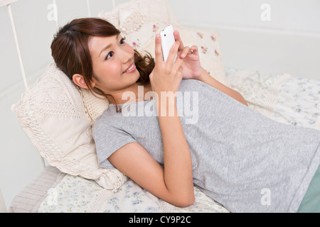 Junge Frau am Bett liegen und auf der Suche nach Smartphone Stockfoto