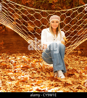 Foto von hübschen Mädchen schwingen in der Hängematte im Garten, nette junge Dame, die Spaß im Freien, schöne Frau mit herbstlichen Blatt Stockfoto