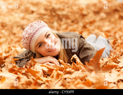 Bild hübsche Frau unten auf dem Boden liegend bedeckt trocken herbstliche Laub im wunderschönen Park, süße Frau, die Spaß im Herbst Stockfoto