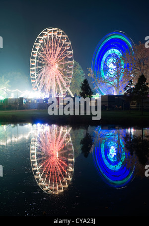 Die Lichter von zwei Riesenräder in einem Vergnügungspark spiegelt sich im Wasser eines Teiches Stockfoto